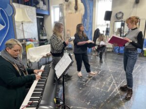 The cast of We're Not Going Back stood around a keyboard rehearsing a song