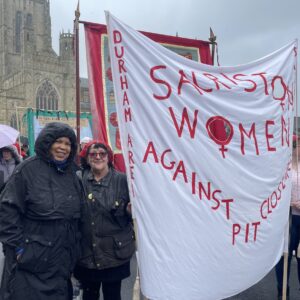 Two women stood in the rain with a banner that reads Sacriston Women Against Pit Closures