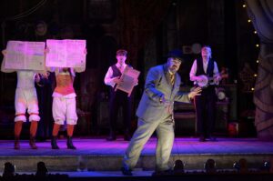 Five people in music hall costume singing and dancing on a stage.