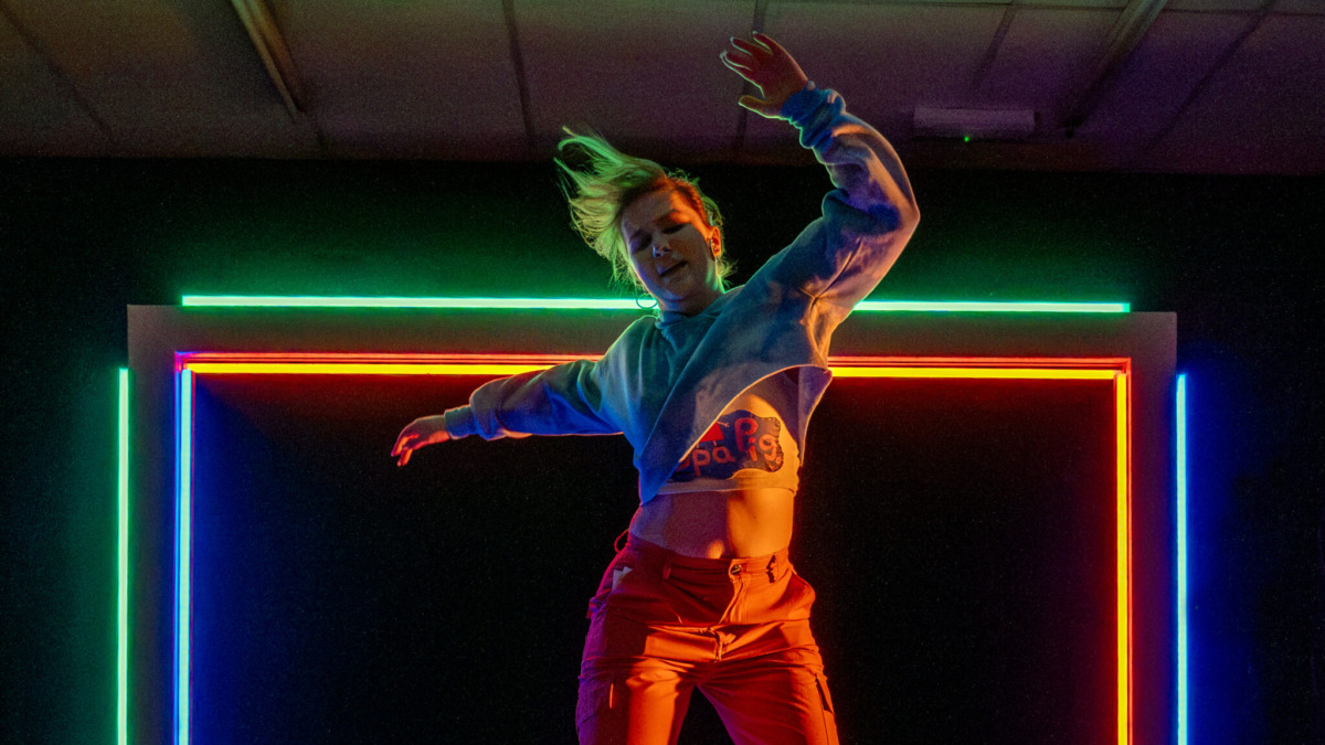A young woman dancing wildly on a table with a neon frame behind