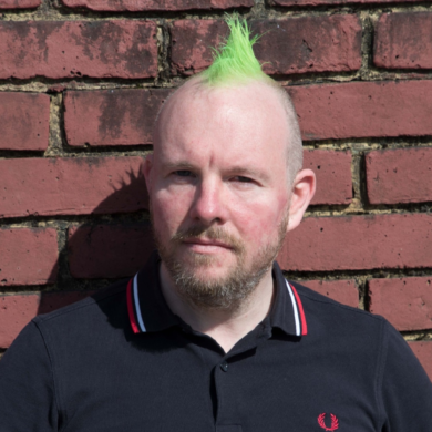 a man with a green mohican against a brick wall