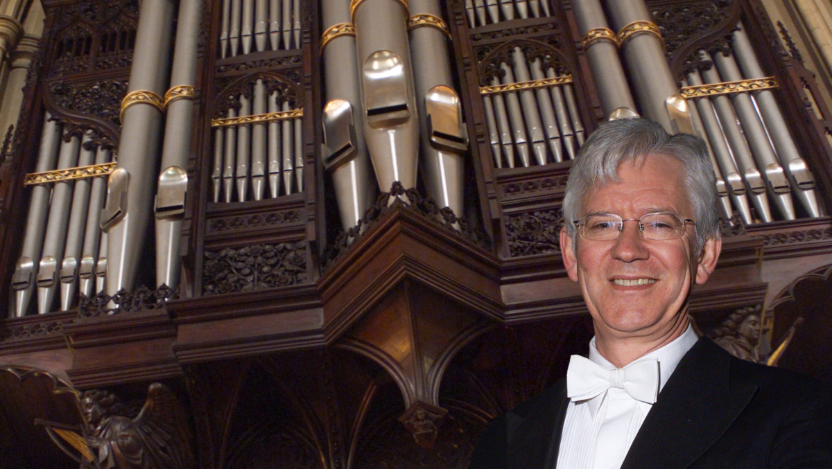 Graham in dress suit stood smiling in front of a large church organ