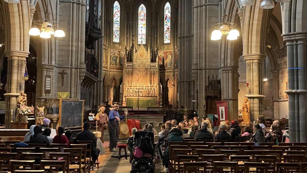 An audience watching a play in front of the stained glass windowns in an 18th century church