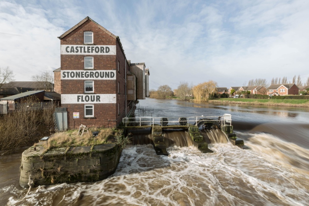 A Yorkhire flour mill on the side of the River Aire with the water gushing past.