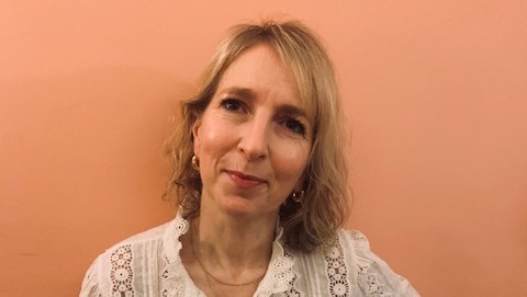 Rose leaning against a peach wall and smiling to camera